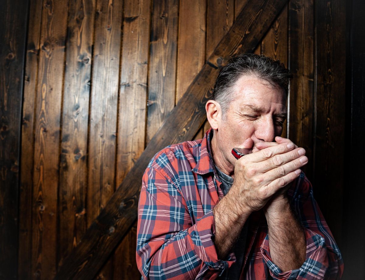 Catfish Jack leaning into a blues harp, hands cupped tight around it to shape the tone