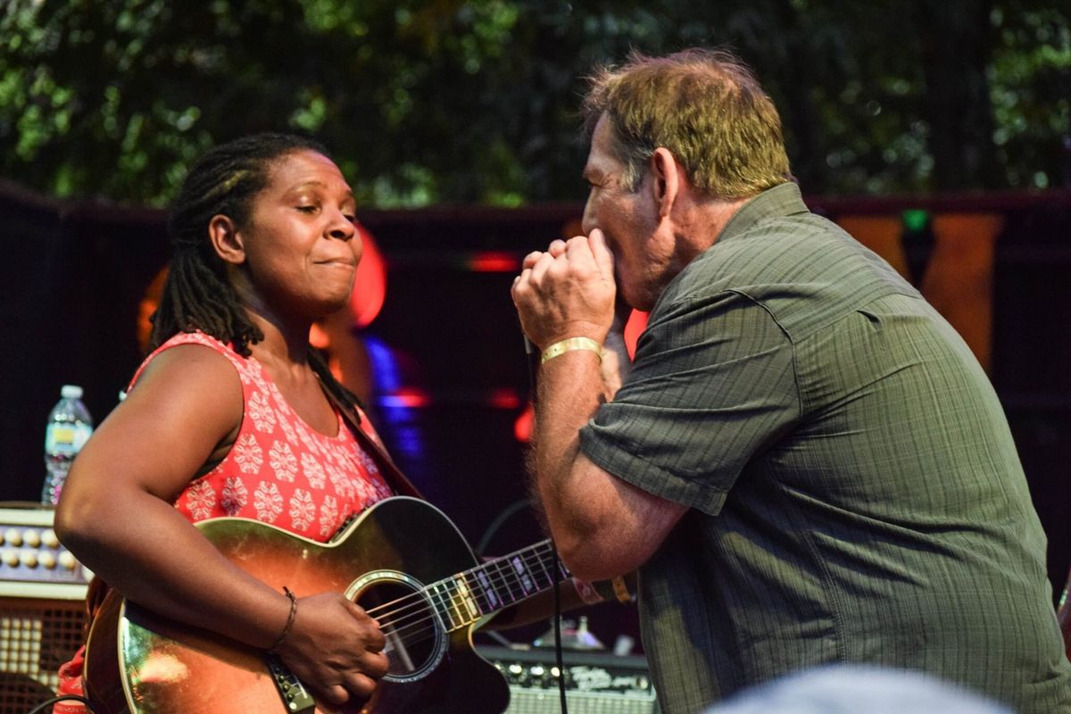 Catfish Jack playing harmonica on stage facing Ruthie Foster, who is playing acoustic guitar